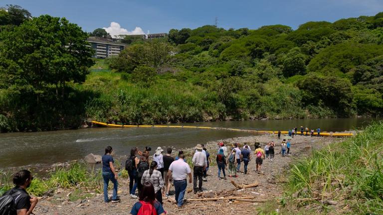 Participantes en la Costa Rica City Academy caminan por las orillas del río Virilla para ver la barrera de plástico que atrapa los residuos.
