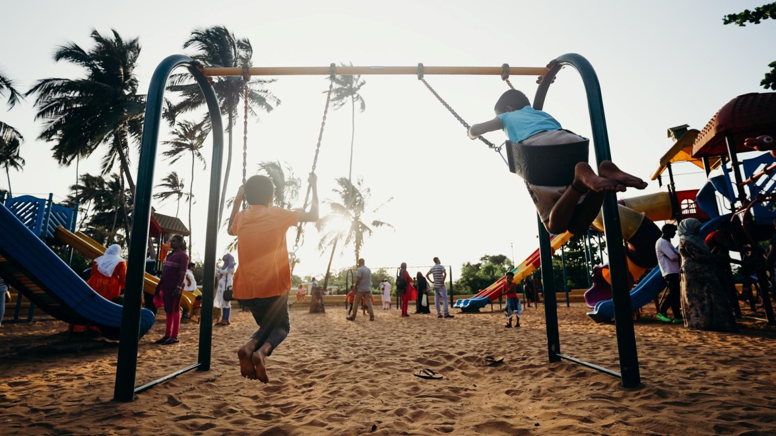 Niños jugando en columpios en un parque de barrio bordeado de árboles