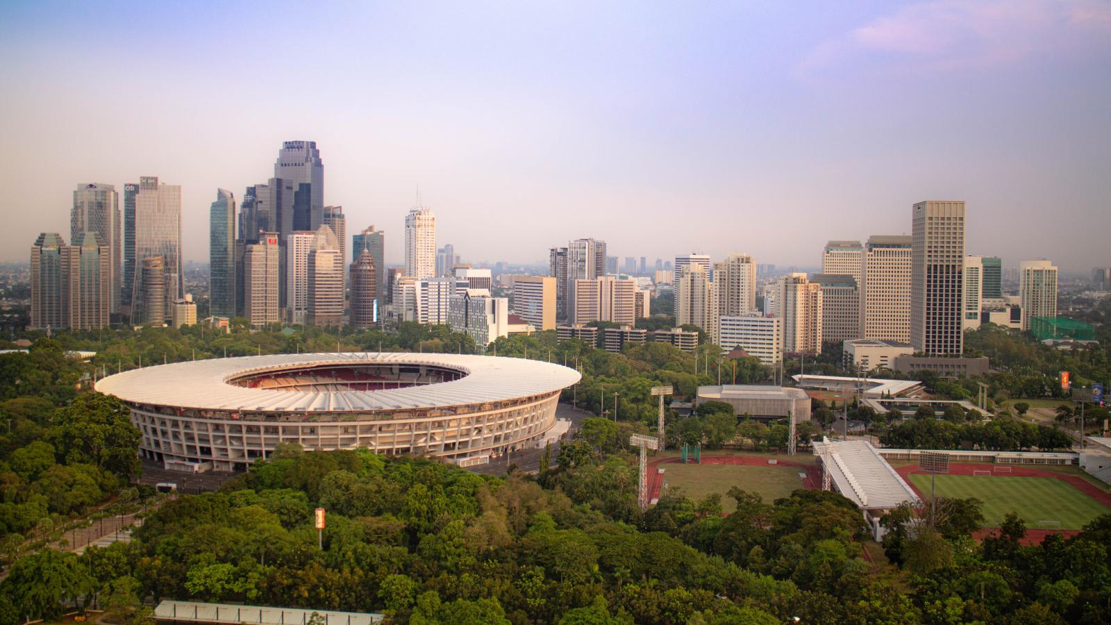 Vista del estadio Gelora Bung Karno de Yakarta rodeado de árboles y del perfil de la ciudad.