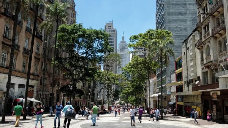 Gente caminando por una calle urbana bordeada de árboles.