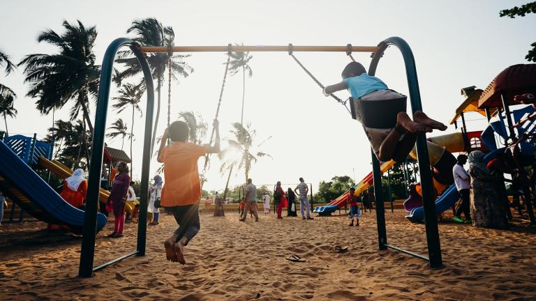 niños en un columpio al atardecer con palmeras al fondo