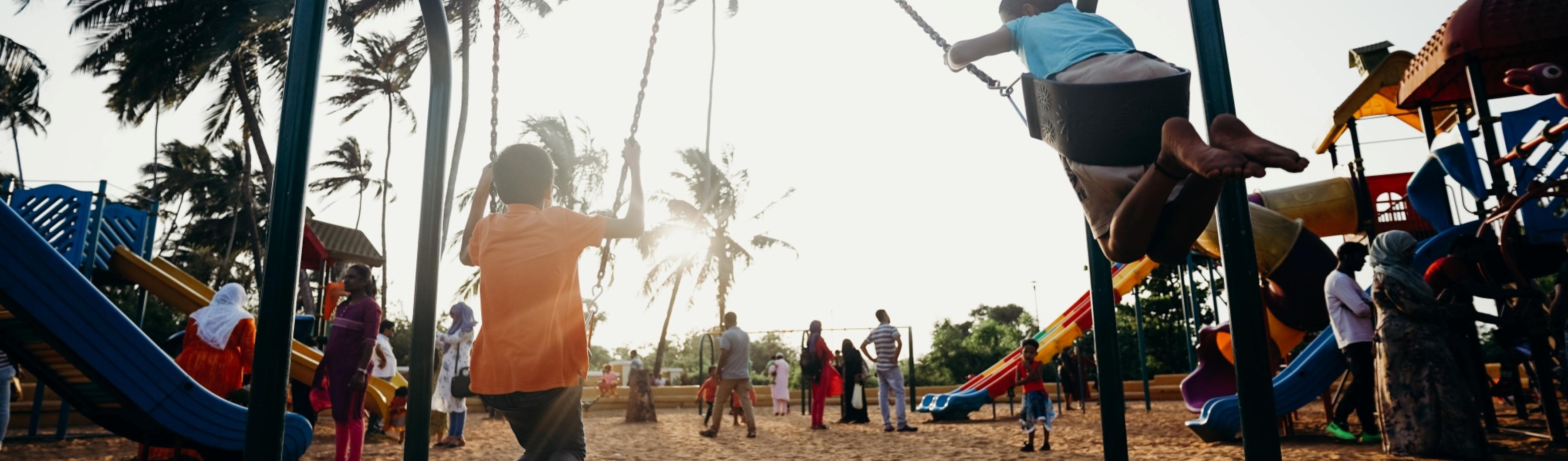Niños jugando en columpios en un parque de barrio bordeado de árboles