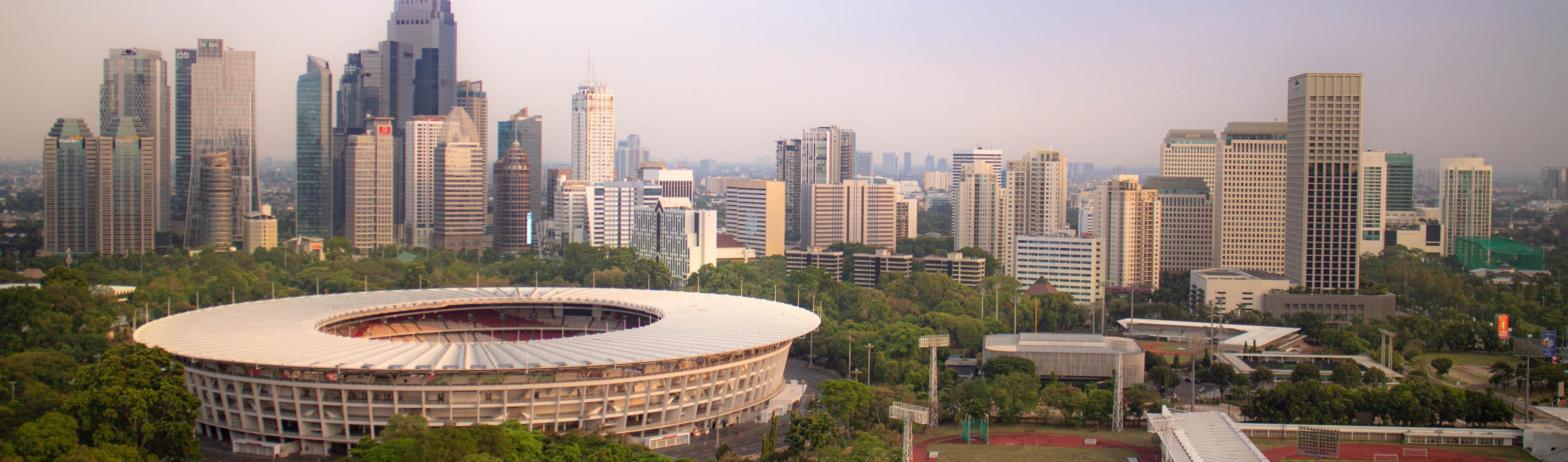 Vista del estadio Gelora Bung Karno de Yakarta rodeado de árboles y del perfil de la ciudad.